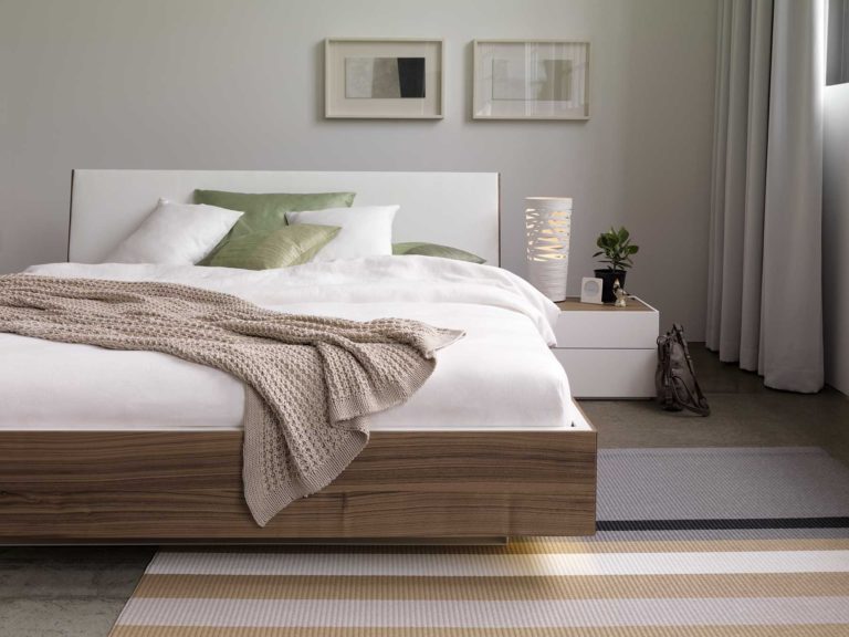 20: Bett mit Kufenuntergestell, kombiniert mit Nussbaumholz und gepolstertem Kopfteil in weiss. Mit sehr schönem Inlay in der Bettkante, ebenfalls in weiss